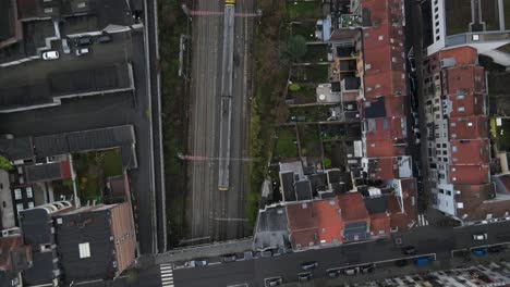 train-drives-along-railroad-across-Brusells-city,-aerial-tracking-view