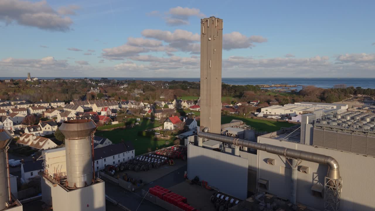 Saint Sampson Guernsey droneoptagelse af kraftværkskompleks og skorsten, der flyver mod Bordeaux Havn i gylden sol med interessant himmel og hav i baggrunden