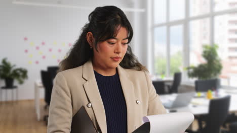 close up shot of businesswoman in modern open plan office looking at clipboard and reading report or document