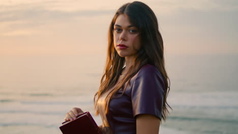 closeup beautiful woman sunset cloudy sky holding book. girl looking camera.