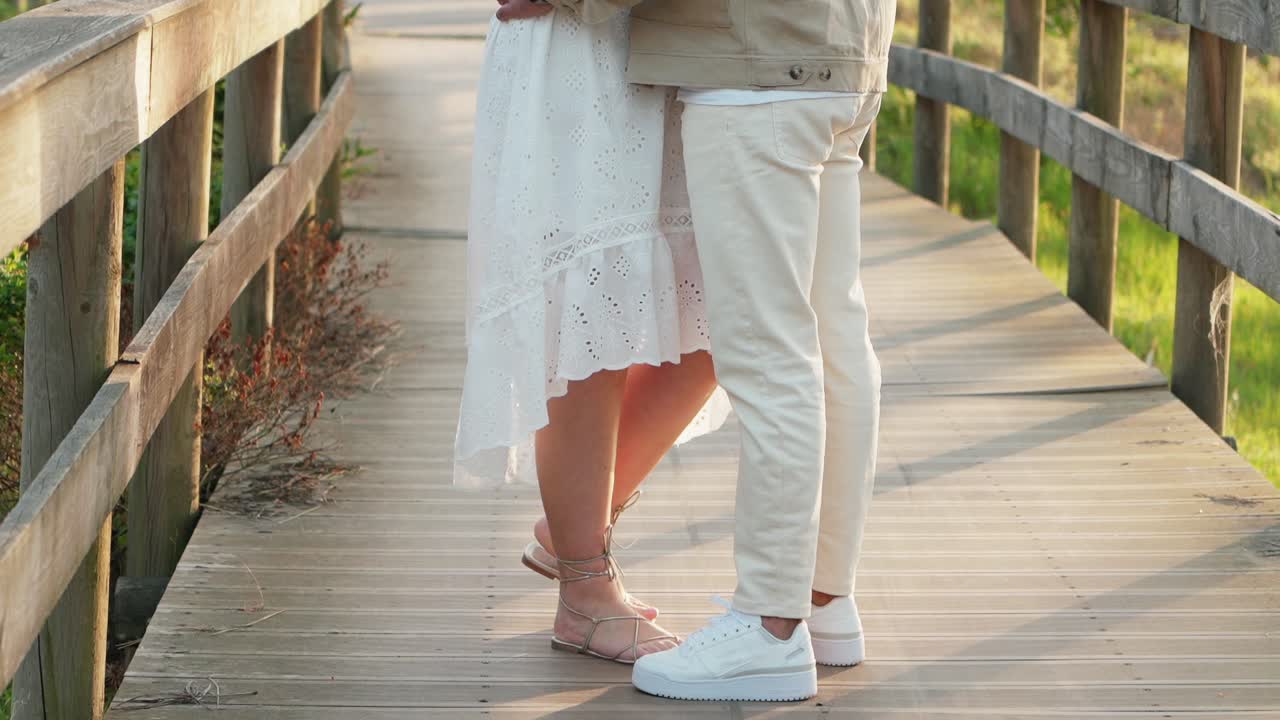couple in white clothes tenderly touching legs on rustic wooden walkway at sunset