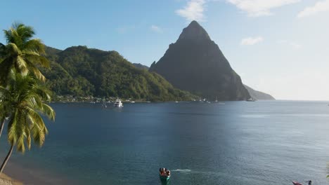 Día-Soleado-En-El-Caribe-Con-Palmeras,-Playa-Y-Picos-Montañosos-En-El-Fondo