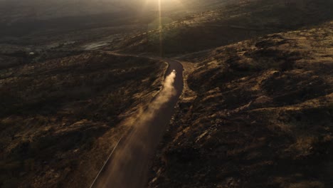 Aerial-view-tilting-toward-a-car-dusting-on-a-dirt-road-in-the-mountains-of-Namibia,-sunset-in-Africa