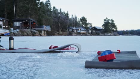 Rubber-Mats-Laid-Down-In-Frosted-Lake-While-Man-Puts-On-Fur-Rug-During-Winter-Fishing-In-Trondheim,-Norway