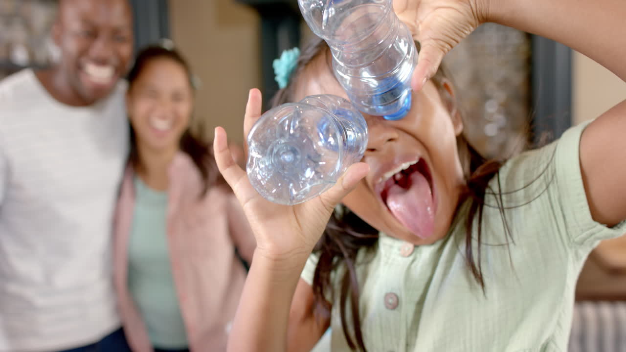 Playing with empty water bottles, girl making funny face with family in background
