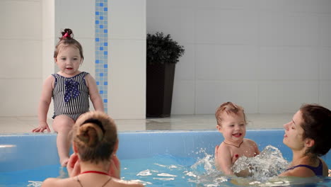 dos bebés se ríen en la piscina y saltan al agua aplaudiendo sus manos