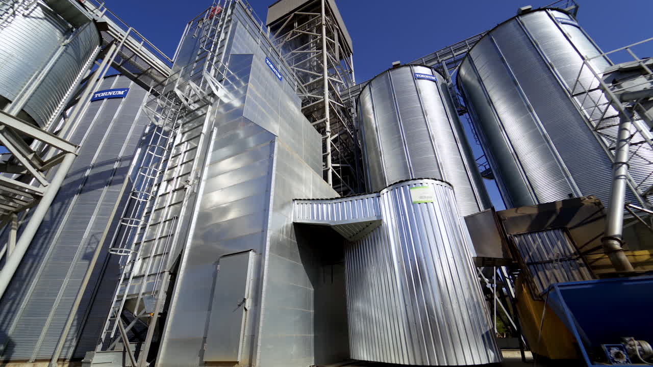 New metal construction of grain elevators. Huge agricultural plant in the countryside. Silver silos for storing crop in bright sunny day.