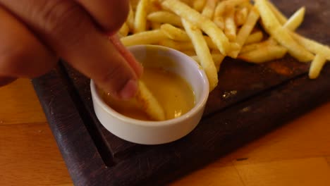 close-up of a hand dipping french fries in mustard sauce