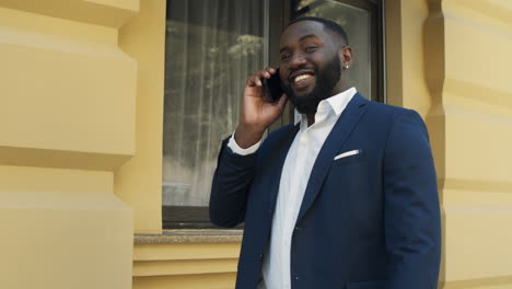 happy african man walking and talking on smartphone on the street