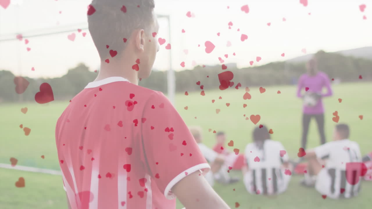 Teenage player standing on soccer pitch, demonstrating sports marketing with floating heart icons
