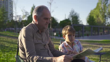 hombre de edad avanzada sentado al aire libre con su nieto leyendo el periódico.