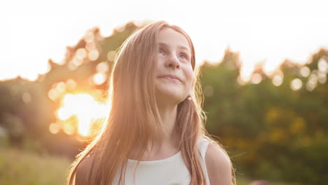 una chica sonriente mirando hacia arriba al atardecer.