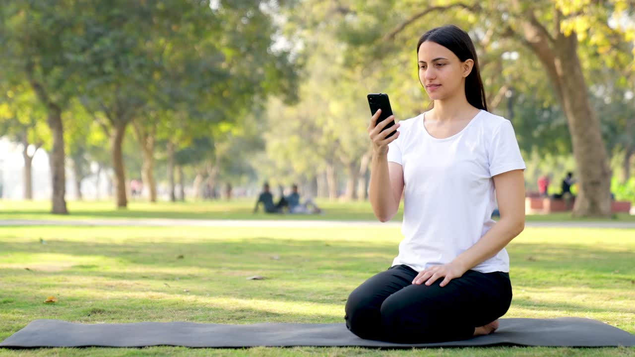 chica de yoga india usando un teléfono móvil en un parque por la mañana