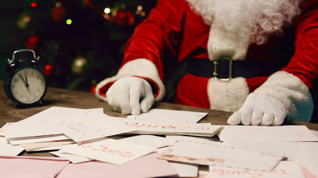 santa claus lee una carta sentado en una mesa en una habitación con adornos navideños