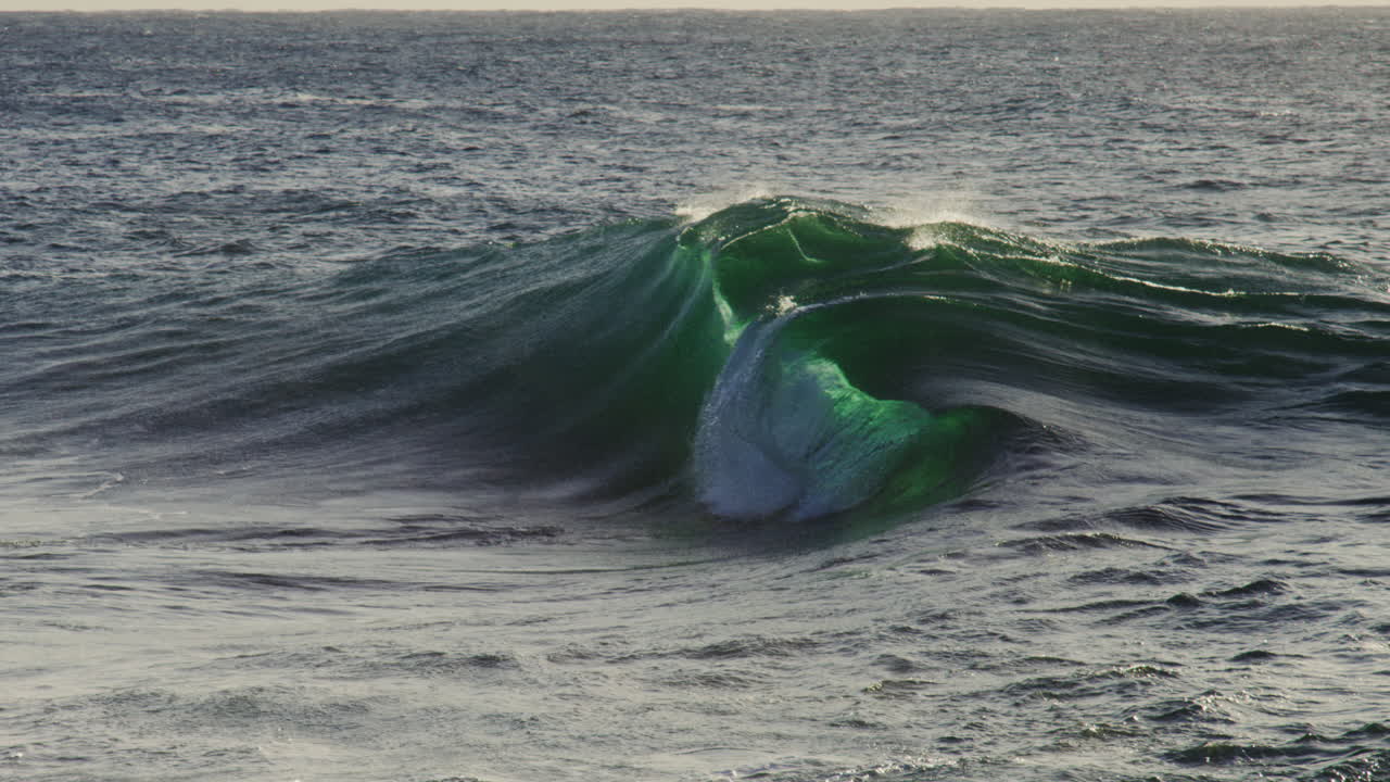 Large swell forms across deep water with blue green gradient and soft foamy details near crest