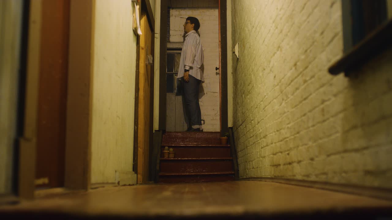 Man walks down apartment hallway and enters door.