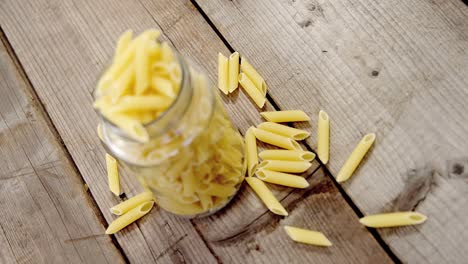 Uncooked-penne-pasta-in-jar-overflowe-on-wooden-table