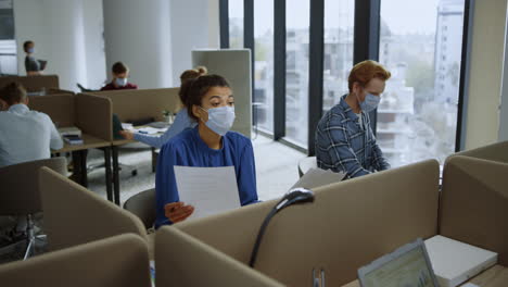 Businesswoman-looking-at-documents.-Professionals-in-masks-talking-in-office