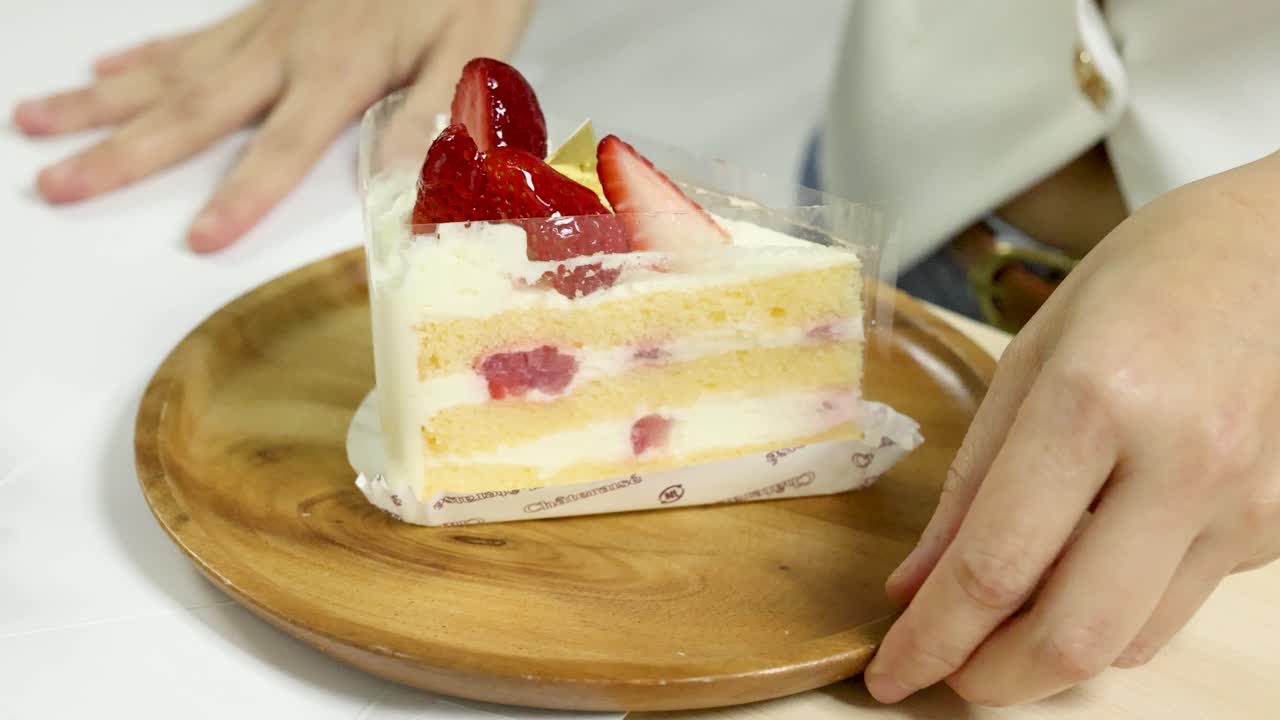 Hand places strawberry cake slice on wooden plate, bright lighting, close-up, steady camera