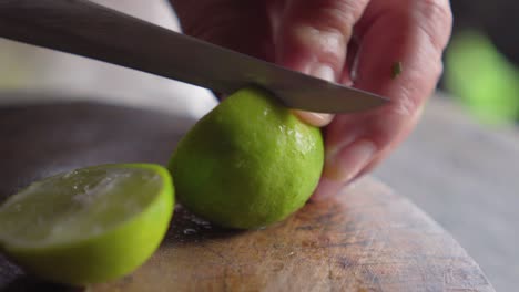 anciana usando un cuchillo para cortar limón verde por encima de la tabla de madera. agua dentro salpicando.