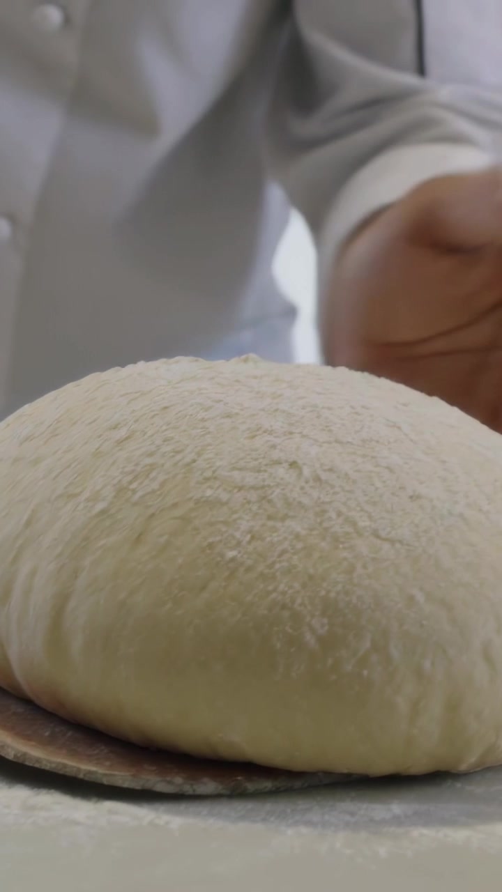 Vertical video: Moving hand, chef in coat checking dough on floured counter, sliding peel to oven