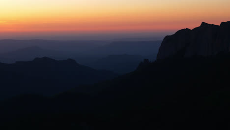 gentle drone dolly forward pass sharp rocky cliff revealing blue hour dusk glow on valley