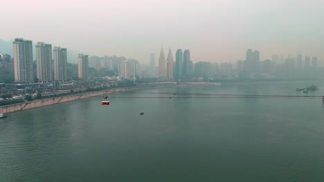 establishing drone shot of chongqing cityscape with cable car above yangtze river during the day in yuzhong district, china