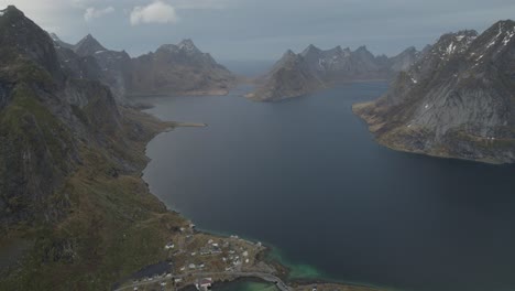 Aerial-view-overlooking-a-town-in-the-Reinefjord,-Lofoten,-Norway---tilt,-drone-shot