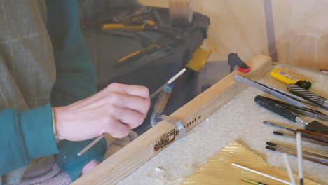 Glass bead maker heating clay and shaping a molten bead with a flame, tools at hand