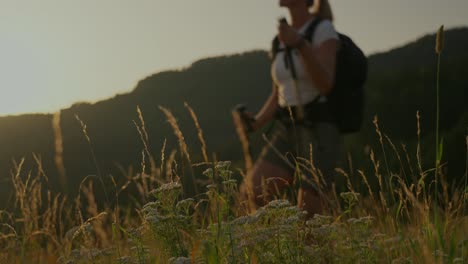 a young couple hikes through a grassy field at sunrise, surrounded by mountains in the distance