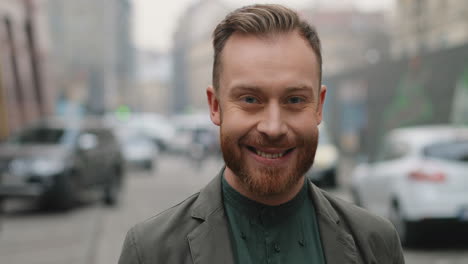 portrait of caucasian stylish businessman standing on the street, looking straight to the camera and smiling