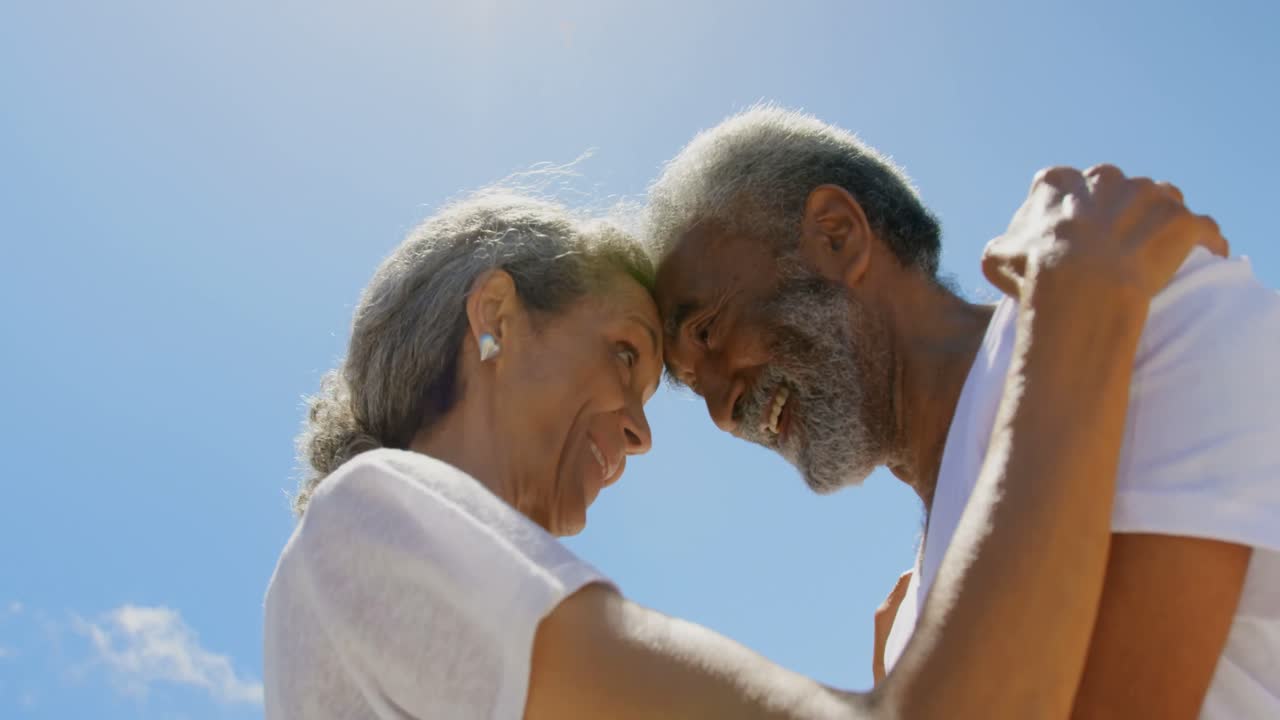 vista de bajo ángulo de una feliz y activa pareja afroamericana de alto nivel abrazándose en la playa bajo el sol 4k