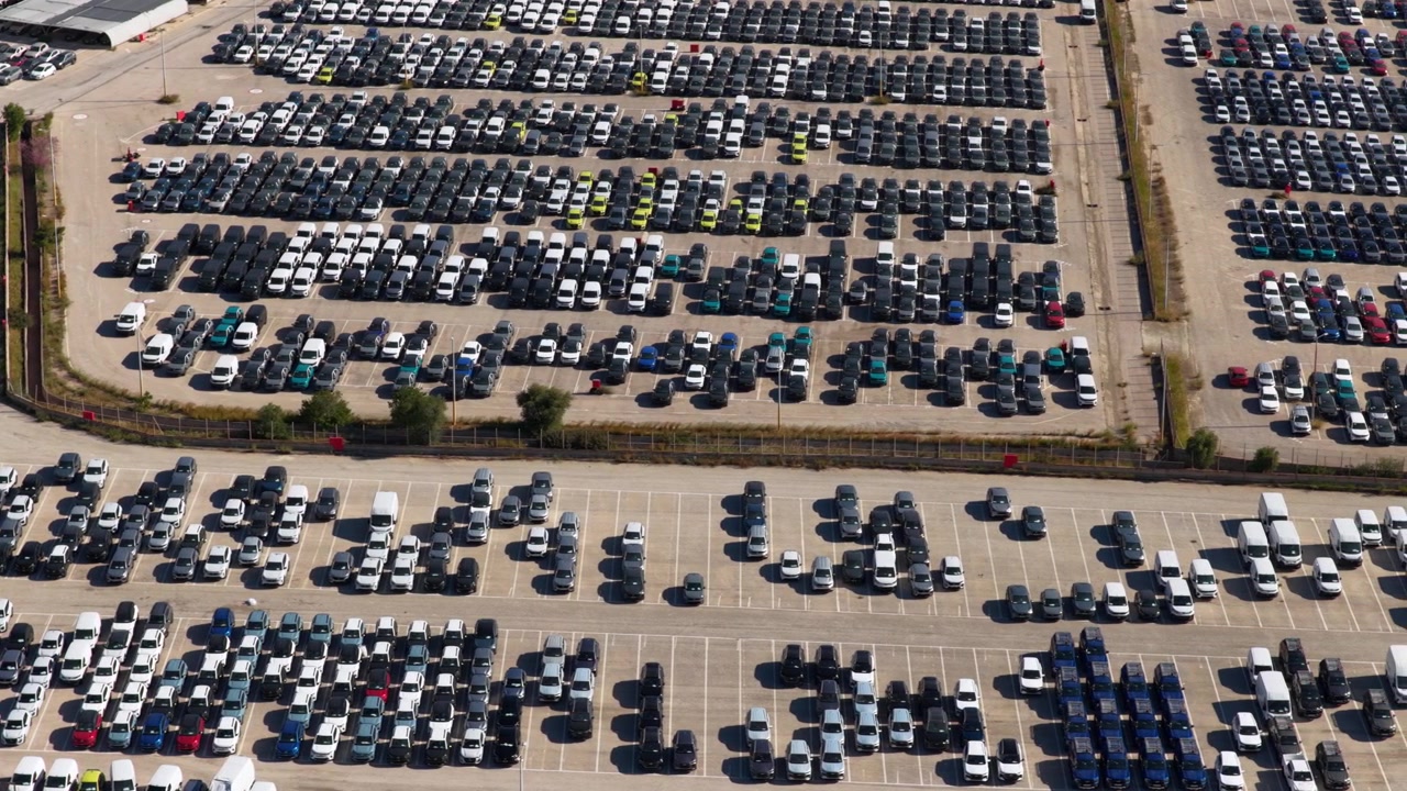Højt luftfoto af en kæmpe parkeringsplads fyldt med utallige nye biler klar til eksport og distribution, der repræsenterer bilindustrien, logistik og masseproduktionskoncepter.
