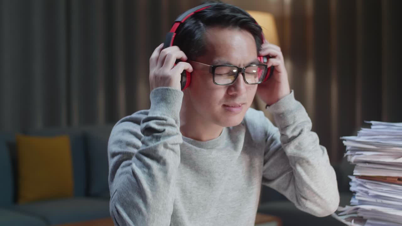 primer plano de un hombre asiático con auriculares y escuchando música después de trabajar con documentos en casa