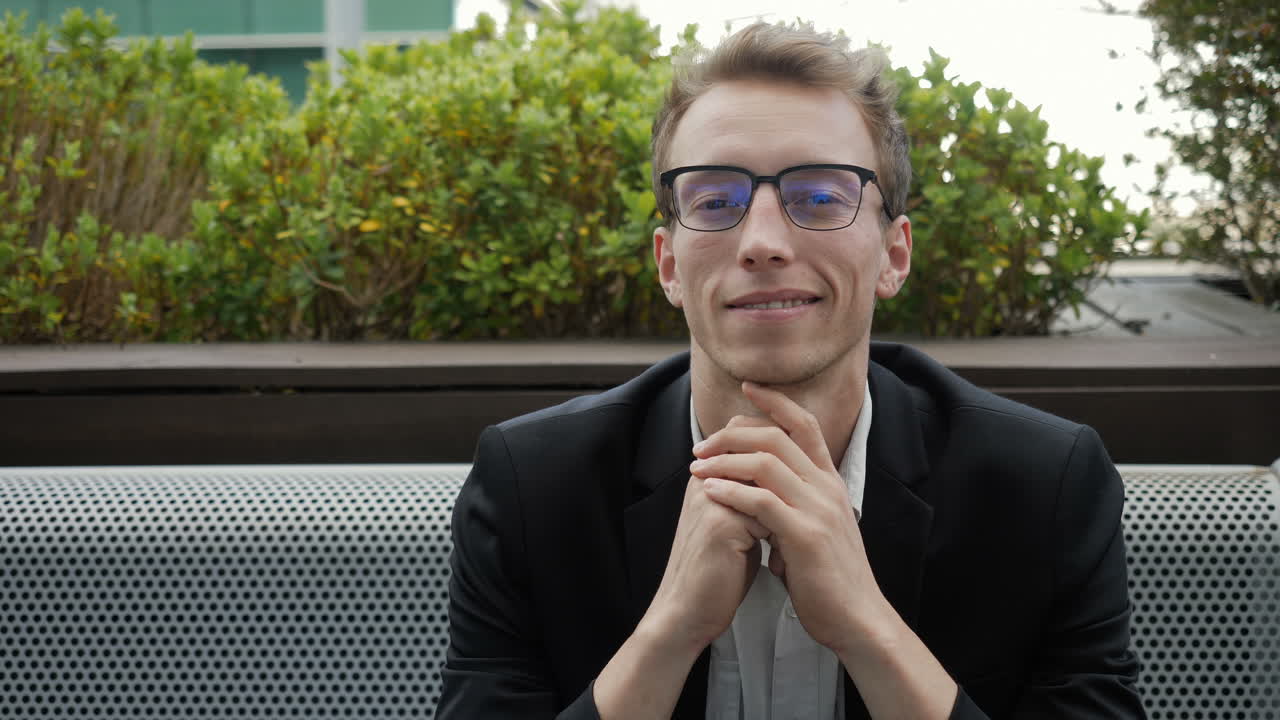 hombre sentado afuera, mirando a la cámara y a un lado, sonriendo