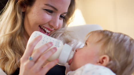 mother in nursery feeding baby daughter from bottle