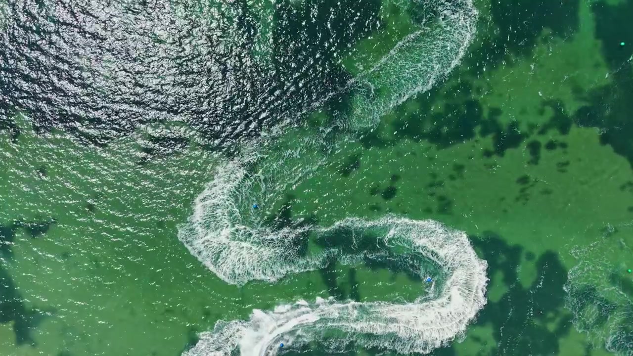 Jet ski racing on a sunny day near the shoreline with smooth water and vibrant green algae patches