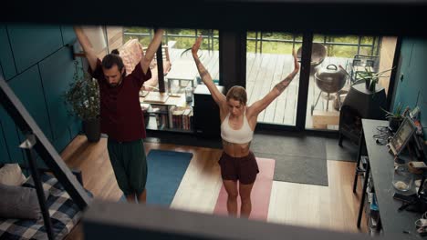 Overview-and-top-view:-a-blonde-girl-and-a-brunette-guy-do-exercises-synchronously-on-special-red-and-blue-rugs-in-a-country-house