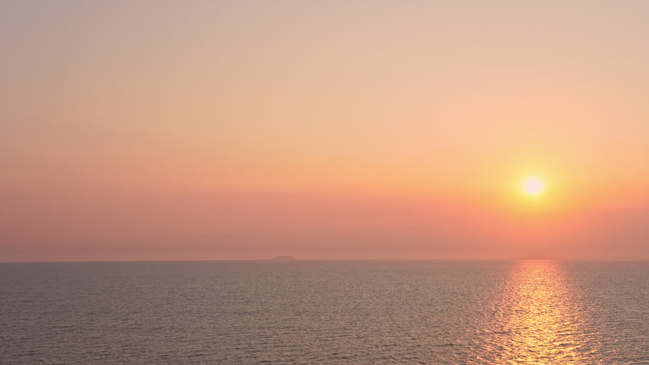 눈부신 주황, 분홍, 빨강, 노랑의 석양이 바다의 지평선 위로 드리워져 있습니다.