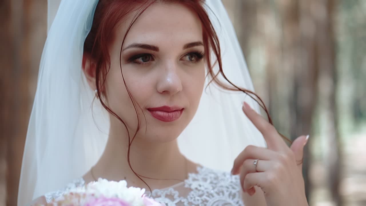 Ritratto di una sposa in un bosco in abito da sposa che si tocca un ricciolo dei capelli, primo piano rallentato