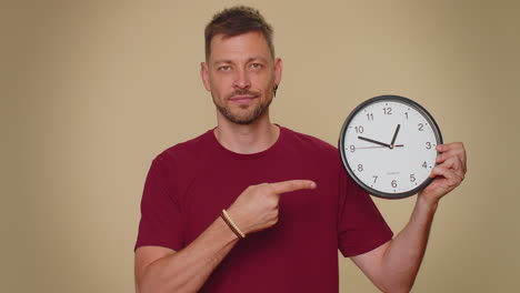 hombre guapo mostrando la hora en el reloj de la oficina de la pared, ok, pulgar arriba, aprobar, señalando con el dedo a la cámara