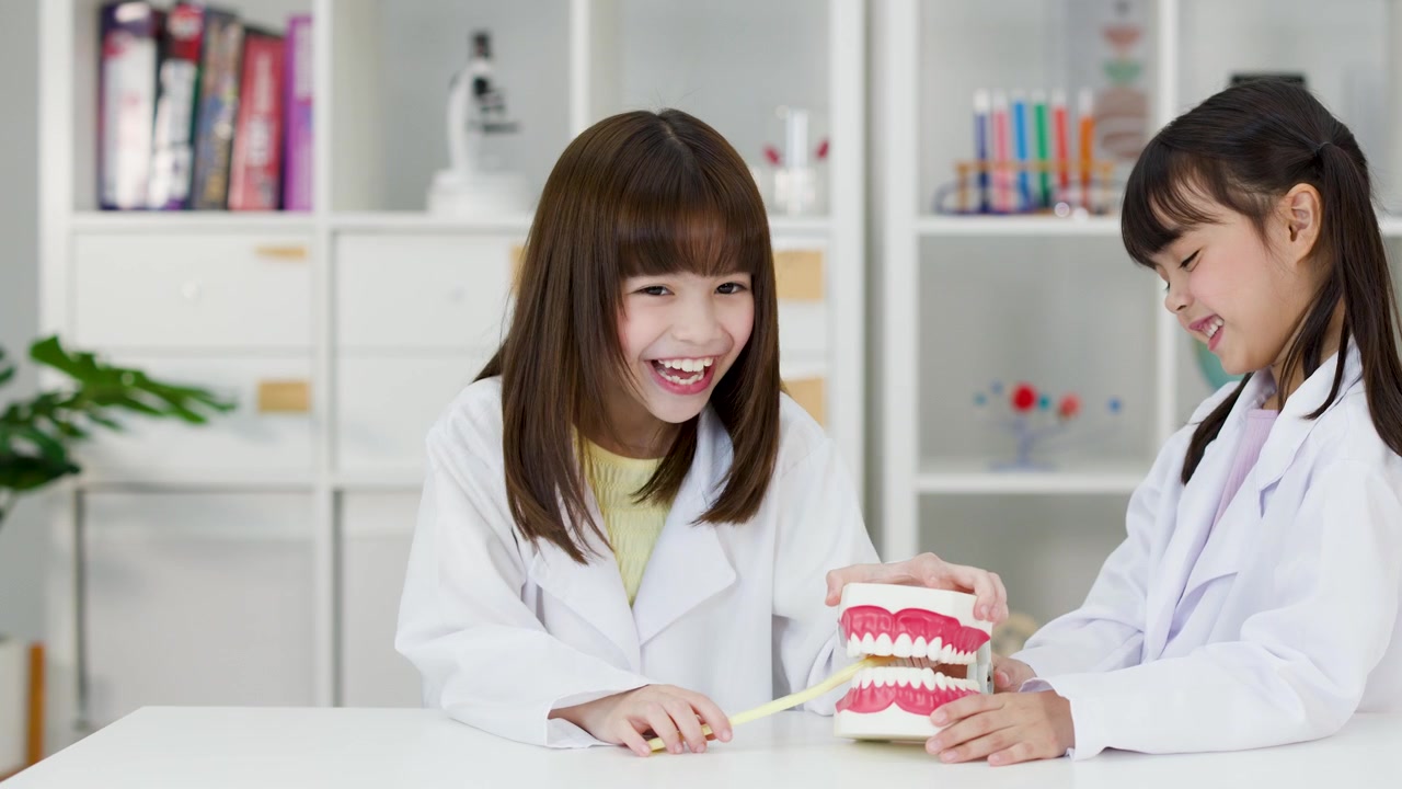 白衣を着た2人の若い学生が、大きな歯の模型を使って歯磨きの練習をしている。