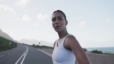 portrait of mixed race woman exercising on mountain road stopping to rest during run