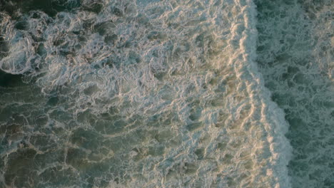 top down aerial shot over white foaming waves in a blue sea at golden hour