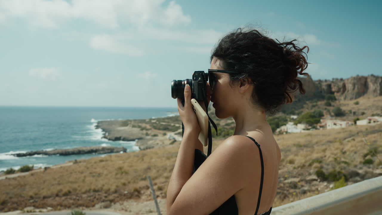 Mujer tomando una foto con vista a la costa en San Vito lo Capo, Sicilia, escena de estilo de vida mediterráneo veraniego