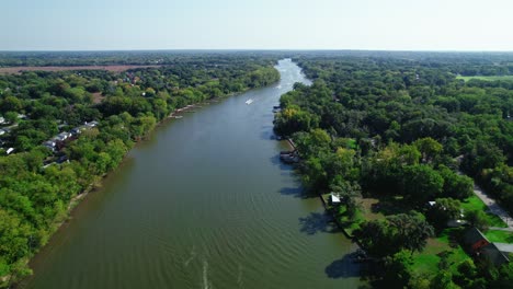 Un-Dron-Aéreo-Captura-El-Río-Fox-Con-Algunos-Barcos-Navegando-Mientras-Serpentea-A-Través-De-Un-Exuberante-Paisaje-Boscoso-En-Crystal-Lake-Illinois,-EE.UU.