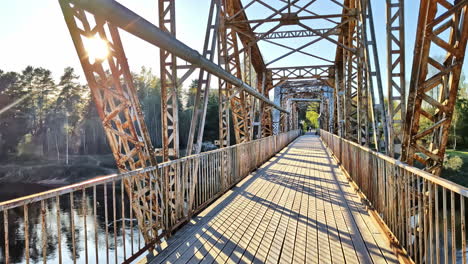 sunlight flares through the steel trusses of a bridge with a wooden pedestrian deck