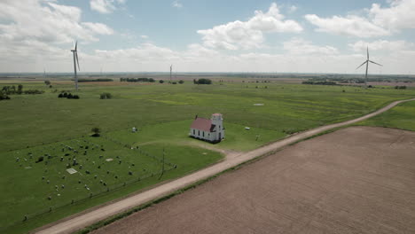 slow aerial approach towards small church, cemetery. wind turbines in background.