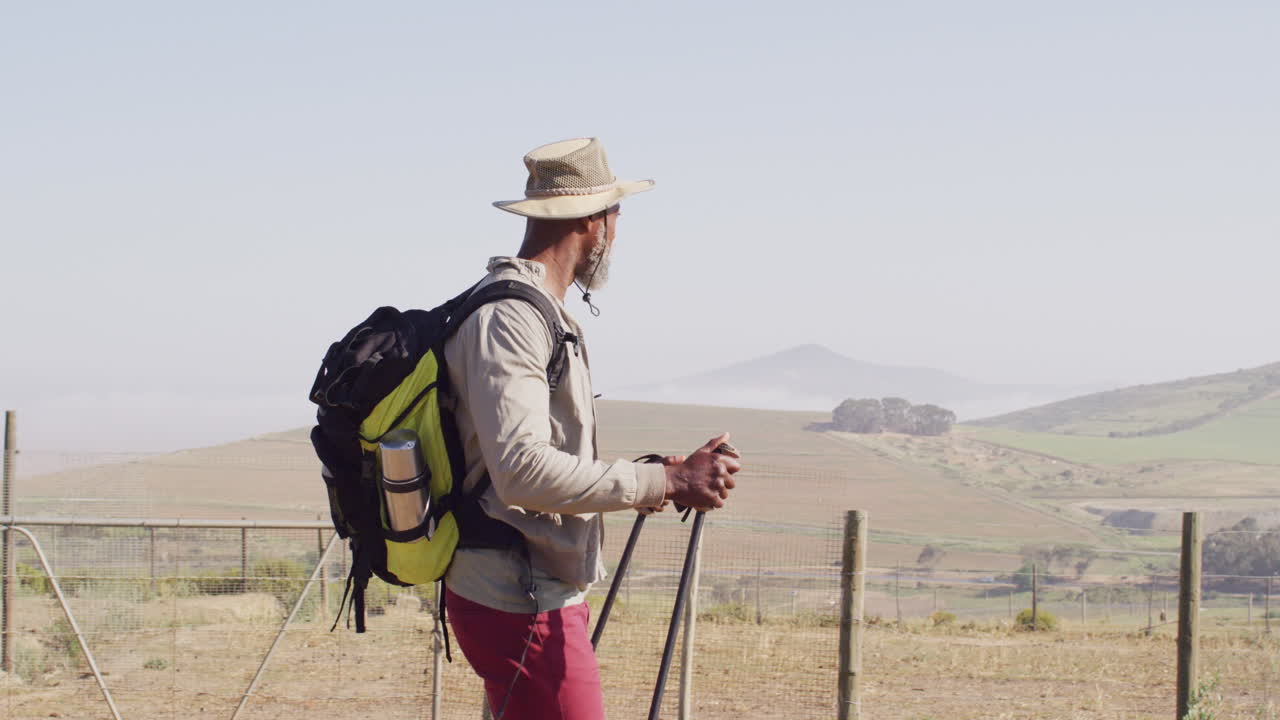 Senior african american man hiking with trekking poles on sunny day, slow motion