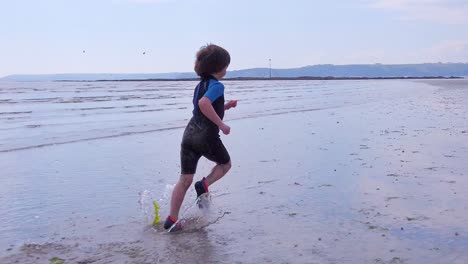 Totale-Aufnahme-Eines-Kleinen-Jungen,-Der-An-Einem-Schönen-Tag-Vor-Der-Kamera-über-Die-Strandbrandung-Davonläuft